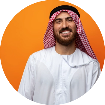 A man in Thobe standing in front of orange wall and smiling brightly