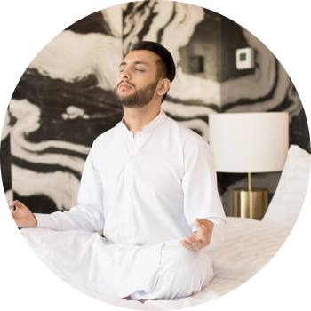 A man dressed in white sits cross-legged with eyes closed and meditating