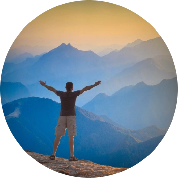 A man with opened arms standing at top of mountain representing the courage to overcome limitations and discover his full potential.