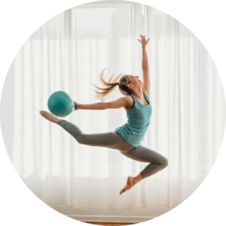 Frau springt mit einem blauen Gymnastikball über dem Kopf und zeigt eine dynamische, selbstbewusste Pose.