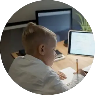 Bambino con capelli biondi che scrive su un foglio alla scrivania.