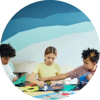 Τρία παιδιά ασχολούνται με χειροτεχνίες σε τραπέζι, καλλιεργώντας τη δημιουργικότητα και τη συγκέντρωση.