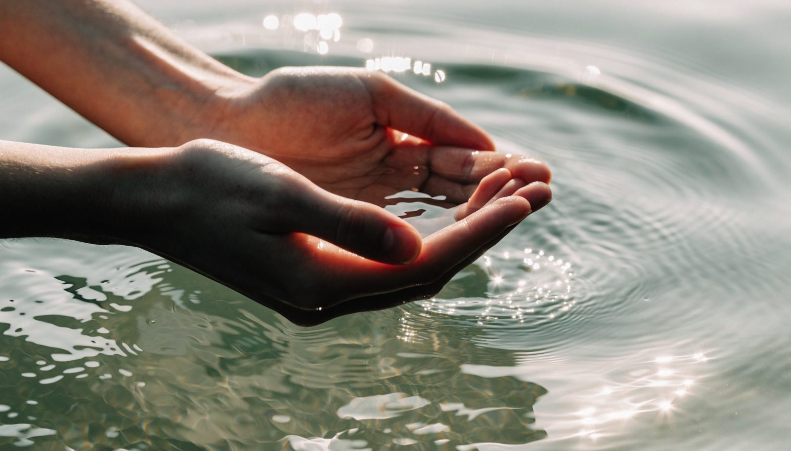 Hände schöpfen klares Wasser im Sonnenlicht