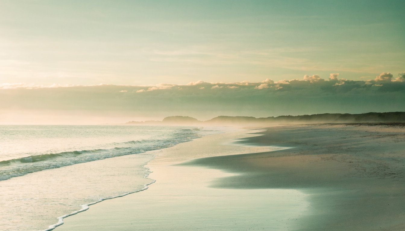 Ruhige Gezeiten steigen und sinken sanft über glattem Sand an einem stillen Strand im Morgenlicht