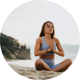 Woman meditating on a beach in a serene setting, embodying the peace and mindfulness taught in the Shakti Kriya course by Art of Living
