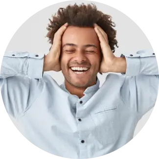 Naeratav mees lokkis juustega, käed peas, väljendab rõõmu ja vähenenud ärevust programmi Art of Living Shakti Kriya raames