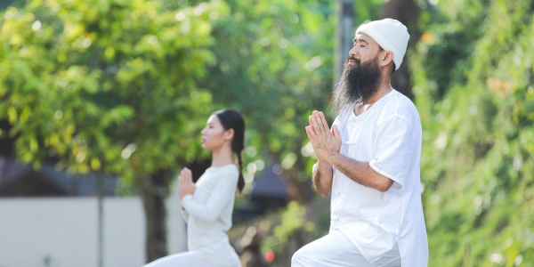 A man and a women dressed in all white cloth, practicing yoga in outdoor space