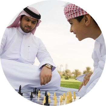 Young man and a boy in white thobe playing chess, focused on developing strategic thinking skills.