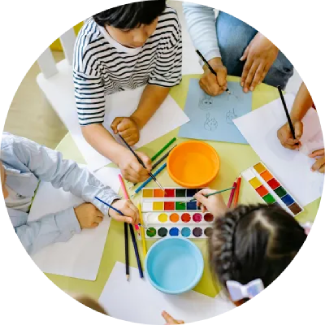 Niños dibujando y pintando en una mesa, representando las habilidades para la vida ART Excel de El Arte de Vivir.