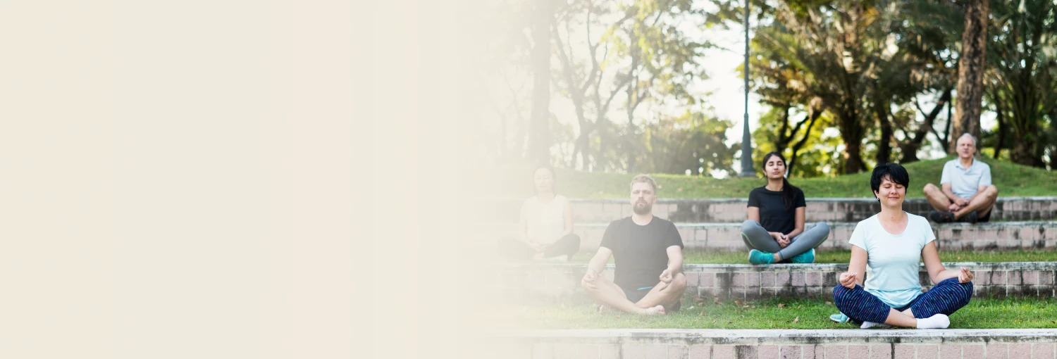 A group of people meditating outdoors on stone steps in a park, sitting cross-legged with eyes closed