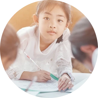 Child with black hair writing on paper at a desk.
