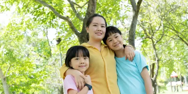 Mother standing outdoors with her two children, all smiling and embracing, symbolizing positive parenting and emotional connection