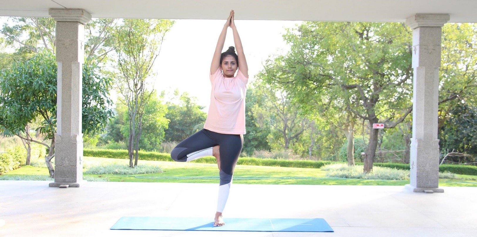 Yoga Vrikshasana - a girl standing with folded hands and one leg bent in tree pose