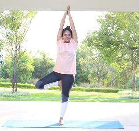 Yoga Vrikshasana - a girl standing with folded hands and one leg bent in tree pose