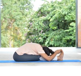 Yoga Paschimottanasana - a girl sitting with stretched legs and touching heals with the hands as in (Seated Forward Bend pose)