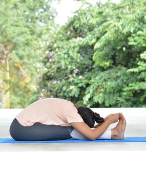 Yoga Paschimottanasana - a girl sitting with stretched legs and touching heals with the hands as in (Seated Forward Bend pose)