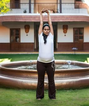 Yoga Tadasana - a lady standing straight with raised hands in tadasana yoga pose
