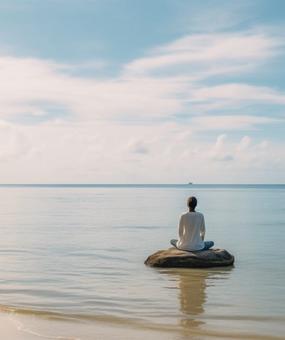 Woman meditating on a rock by the beach facing the water