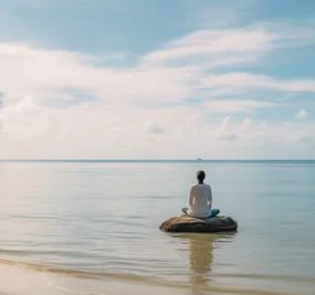 Woman meditating on a rock by the beach facing the water
