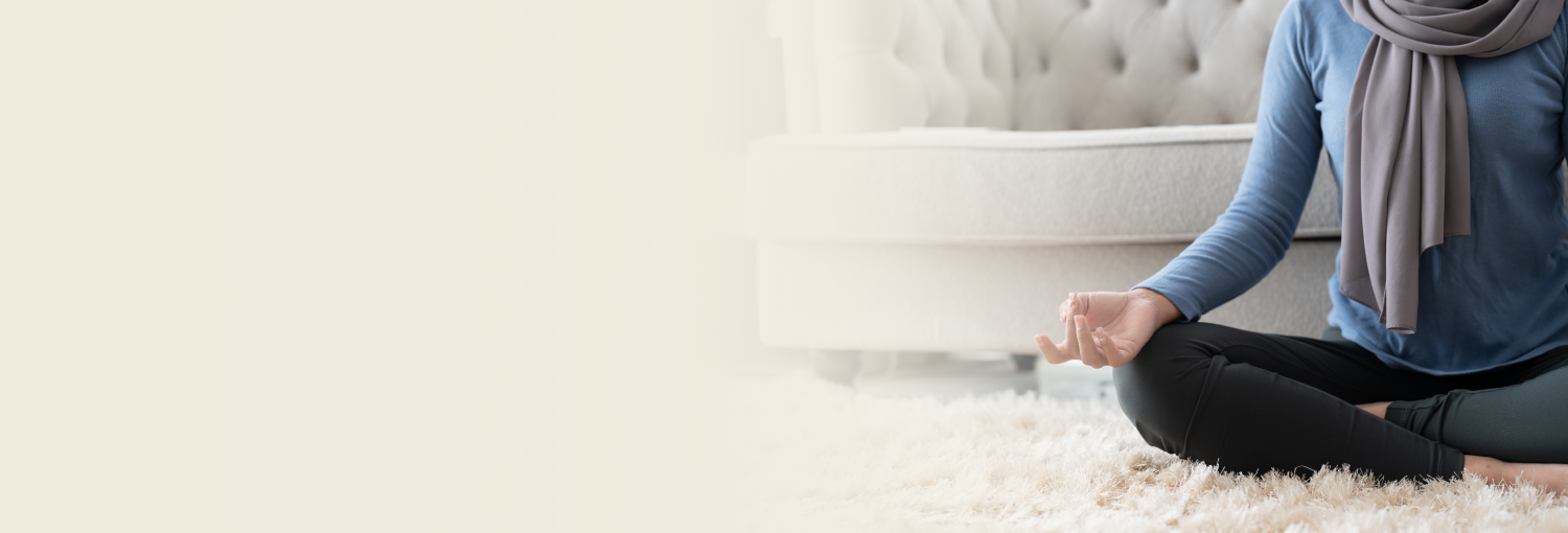 Woman wearing a hijab sitting cross-legged and meditating indoors