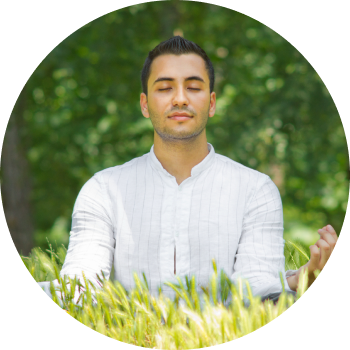 A man dressed in white sits cross-legged in a garden with eyes closed and meditating