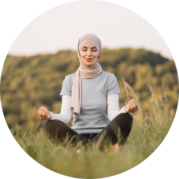 A young woman sits cross-legged on an open field, eyes closed in meditation