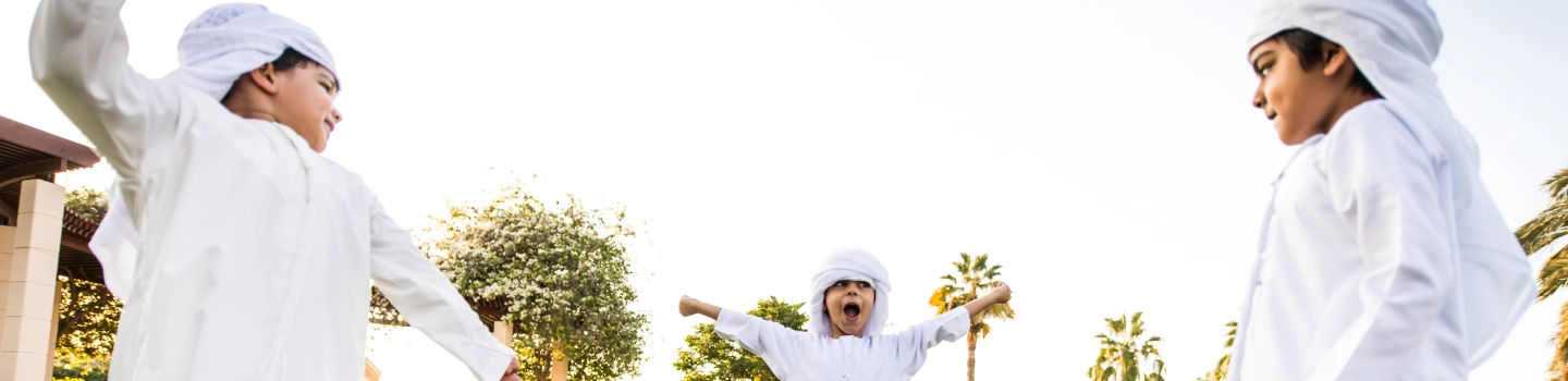 Three children in thobe playing with footlball in grass field 