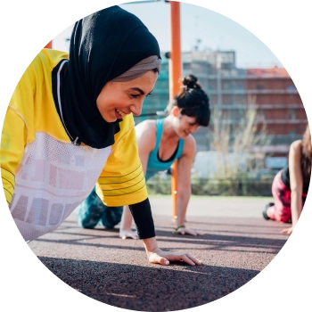 A smiling woman in black hijab and yellow t-shirt performs plank pose in outdoors