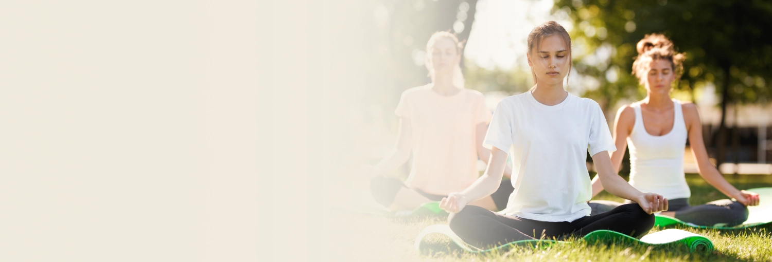 A group of people meditating indoor, sitting cross-legged with eyes closed
