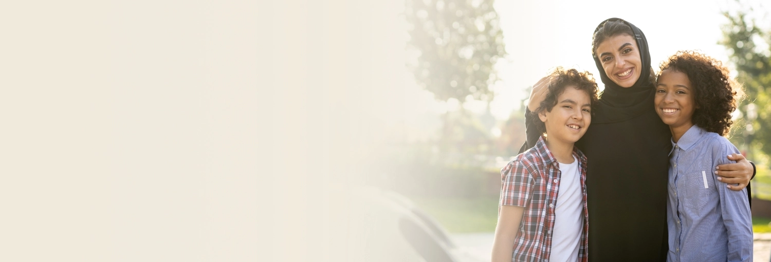 A mother in black burqa standing with her two kids, all three smiling joyfully