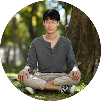 A young woman sits cross-legged on a colorful mat in a peaceful outdoor setting, eyes closed in meditation