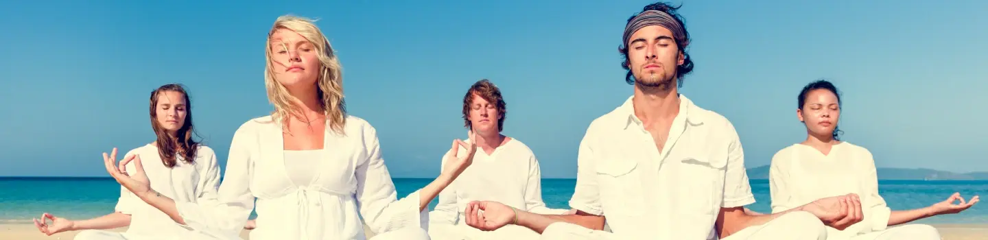 A group of people practicing meditation on the beach as part of the Shakti Kriya course, led by Art of Living