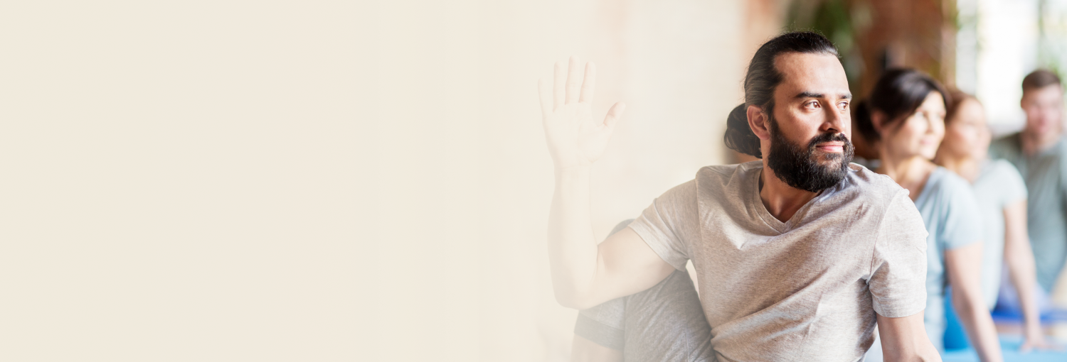 Two women practicing seated yoga poses with hands in prayer position on a grassy field