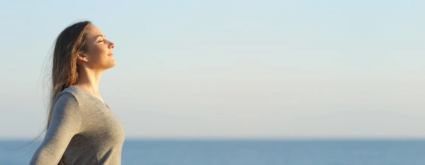 Woman with closed eyes facing the sun in a peaceful moment during an introductory workshop for the Happiness Program, demonstrating mindfulness and presence