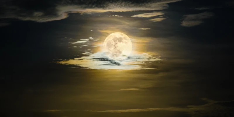 Dramatic night sky with a luminous full moon shining through golden clouds, creating a serene atmosphere perfect for meditation practices