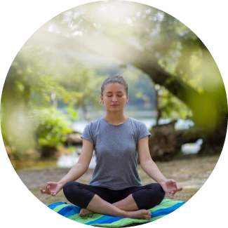A young woman sits cross-legged on an open field, eyes closed in meditation