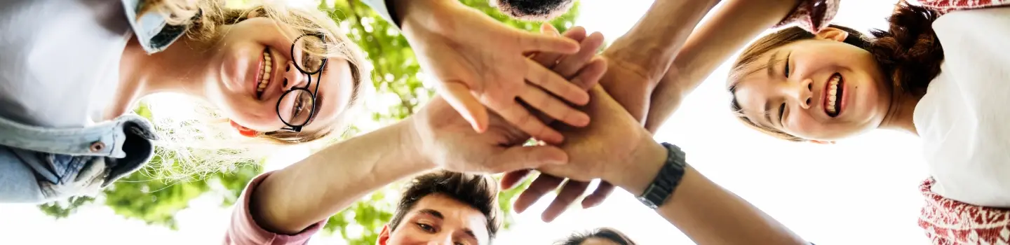Diverse group of teenage friends smiling with hands stacked together, symbolizing friendship and connection