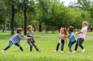 Team Spirit and Fun – Outdoor Youth Activities Children joyfully playing tug-of-war in a green park, representing teamwork, energy, and active participation in youth programmes