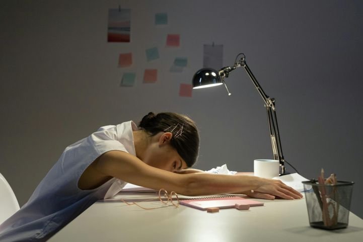 A woman hunched over her desk due to sleep loss.