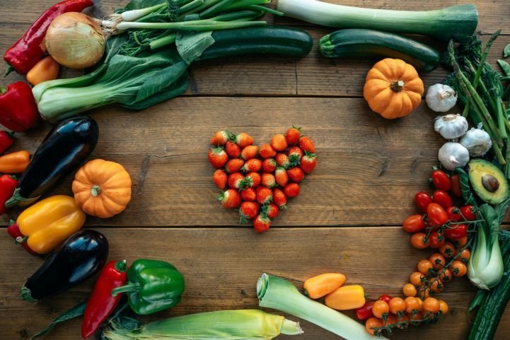 An assortment of veggies and fruits in a circle with strawberries in the shape of a heart for a healthy diet.