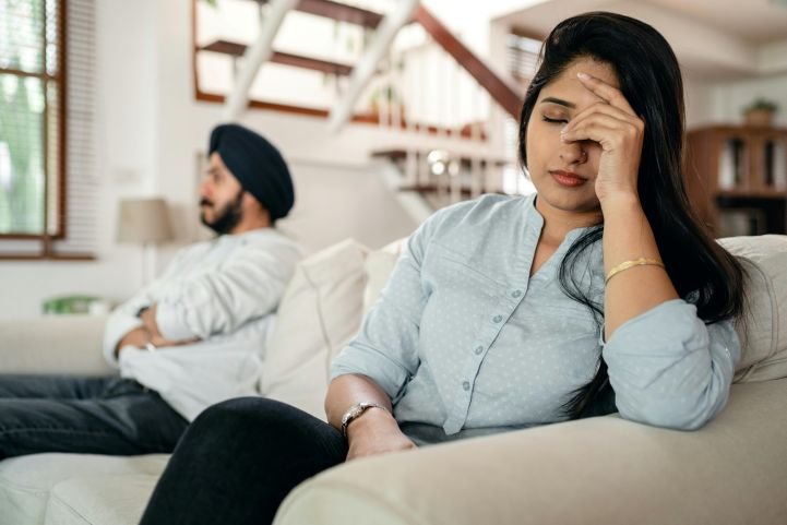 A couple sitting separately on a sofa experiencing chronic stressful situations.