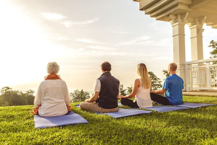 A small group of SKY Breath Meditation practitioners sitting on yoga mats outside facing the view of the sky.