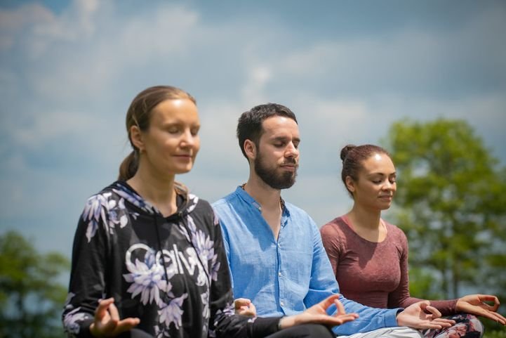 Two females and a male are practicing SKY Breath Meditation outside.