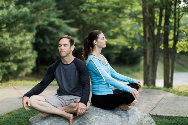 A mom and dad practicing SKY Breath Meditation outside.