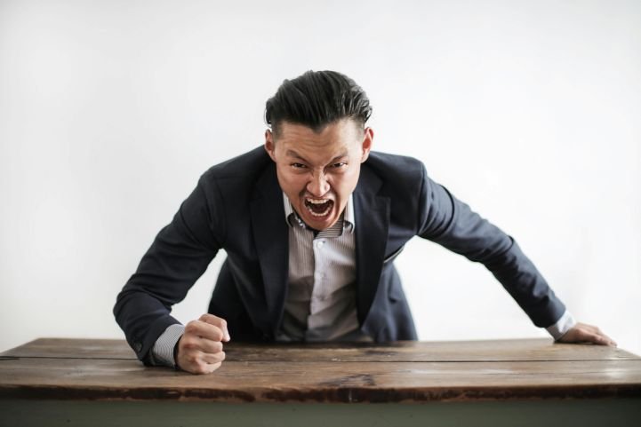 A man is experiencing an angry outburst, slamming his fist on a wooden surface.