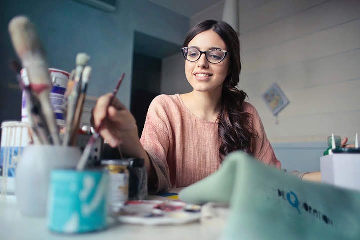 A woman wearing glasses, painting, and enjoying creative expression for mental health.