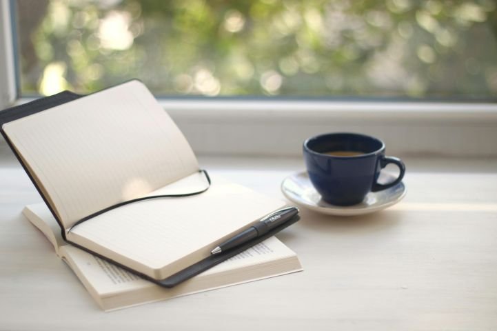 Journal, coffee mug, and open window with natural light for morning routine visualization.