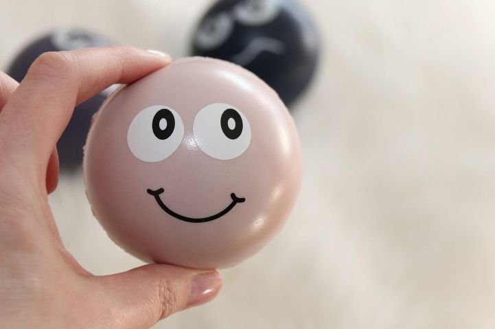 A person holding a stress ball with a smiley face on it.