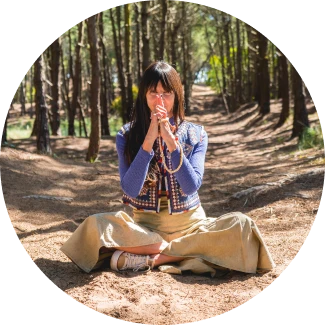 A woman in prayer pose, sitting in a foreset setup 