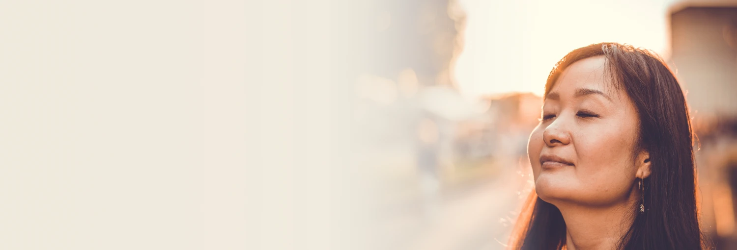 Một người phụ nữ với mái tóc dài và đôi mắt nhắm nghiền đang hít thở không khí trong lành một cách yên bình vào giờ vàng với nụ cười nhẹ nhàng.